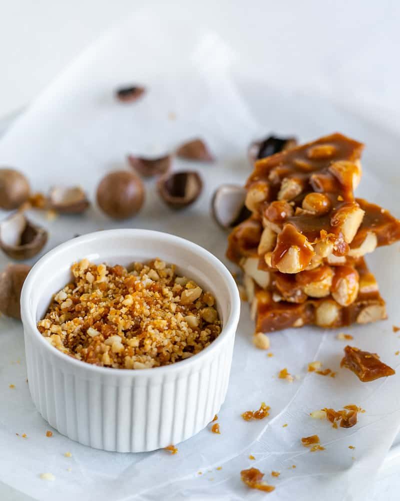 Crispy macadamia nut brittle crumble in a white bowl with a small stack of brittle next to it