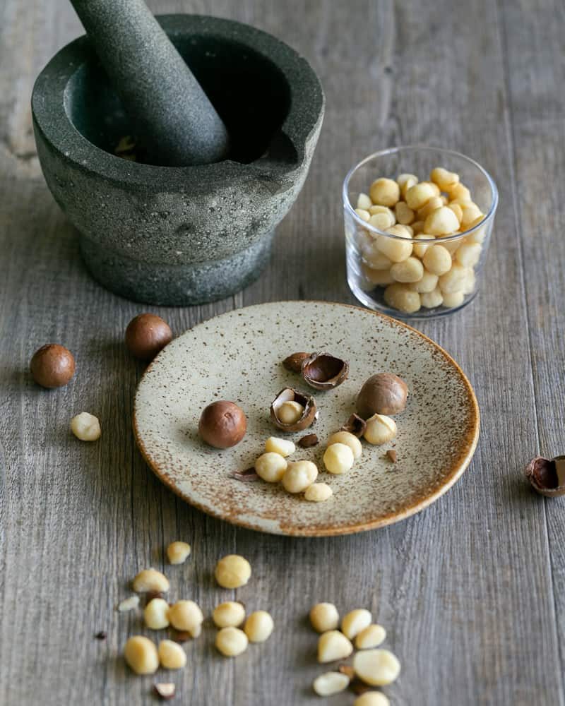 Cracked whole Macadamia showing nut on a small ceramic plate with a mortar pestle in the background